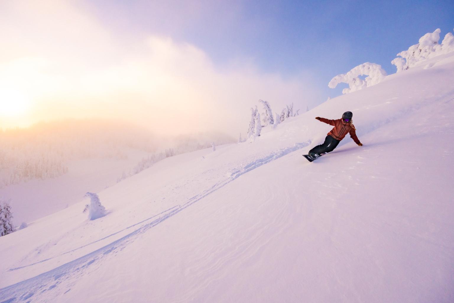 Snowboarder riding powder with a pink sunset in the background