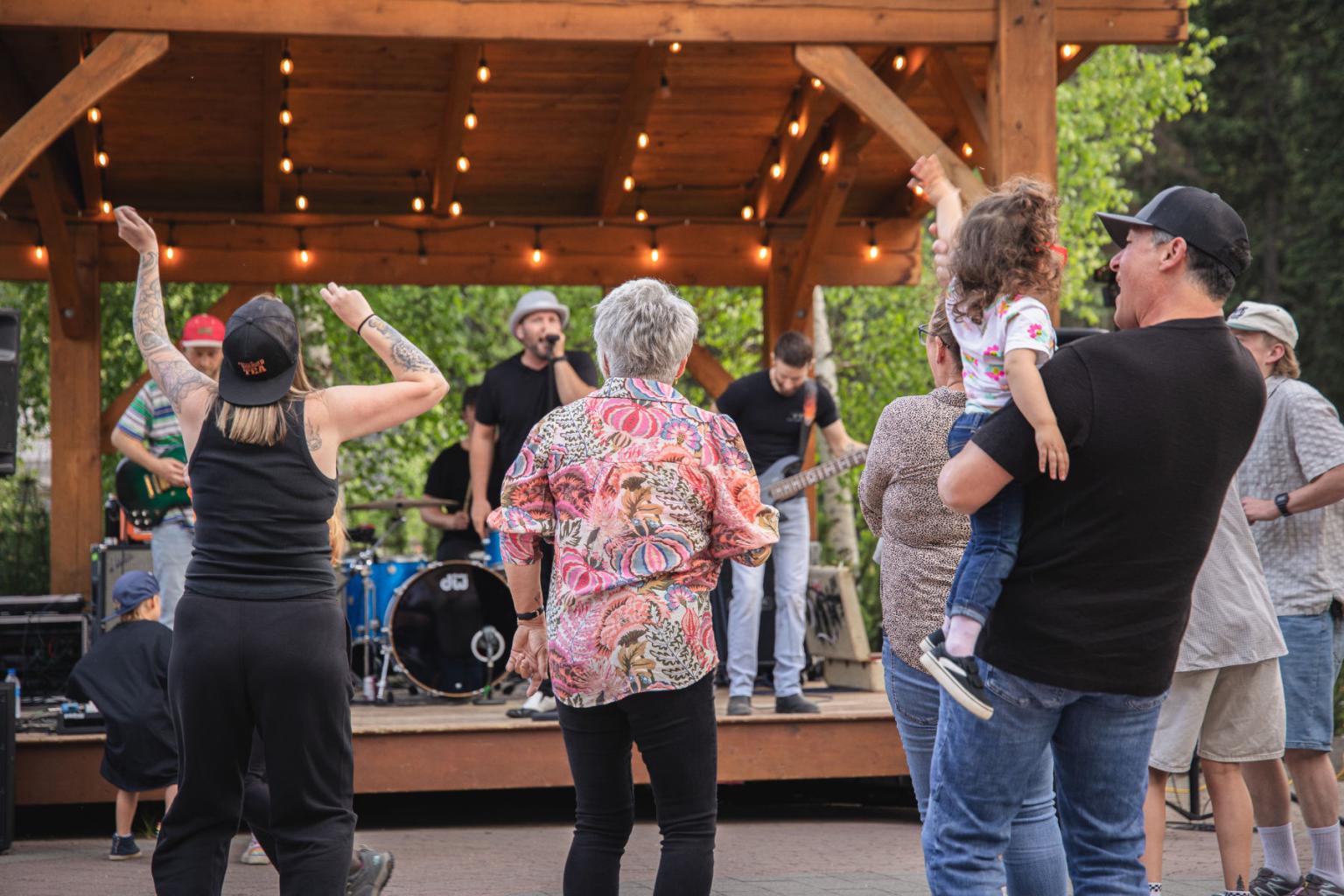 People dancing at an outdoor concert under string lights.