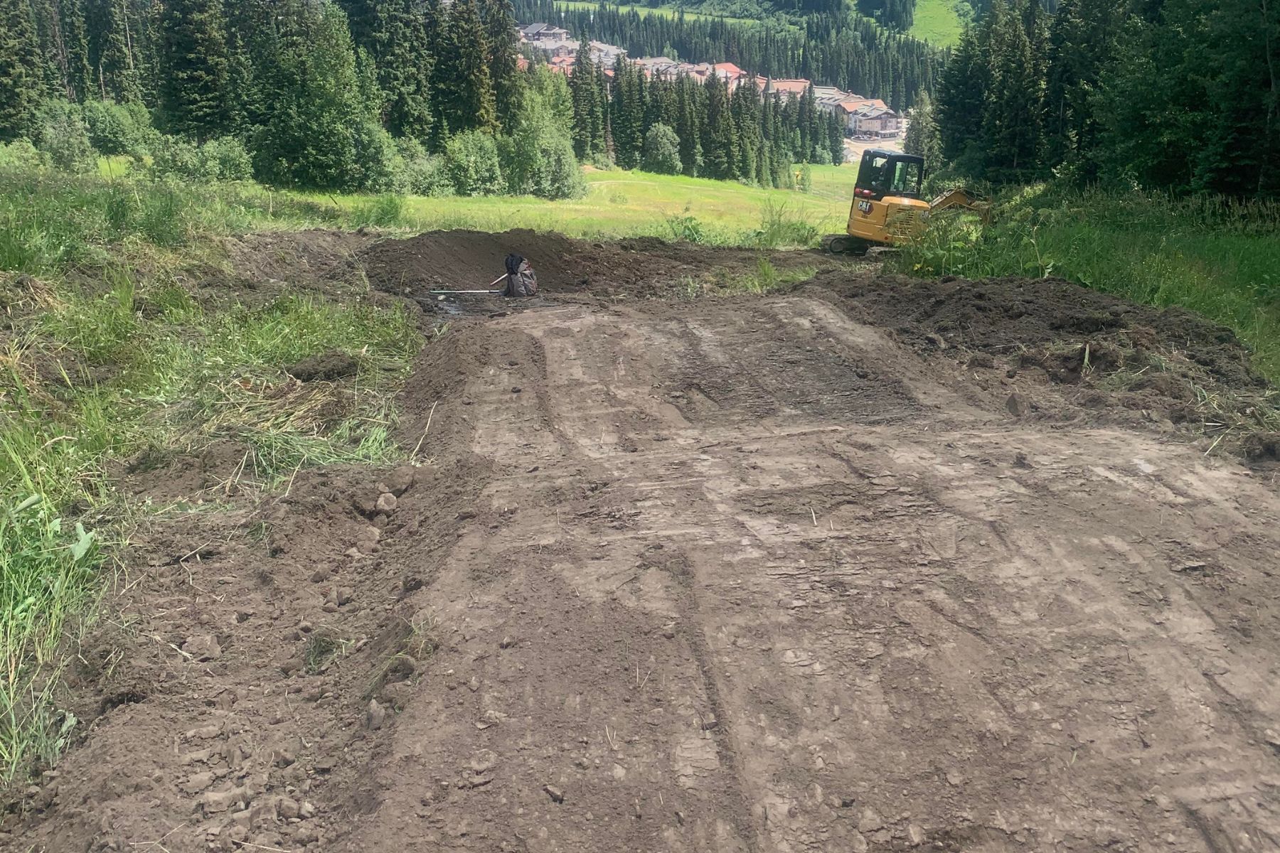 Excavator working on a trail with the village in the background.