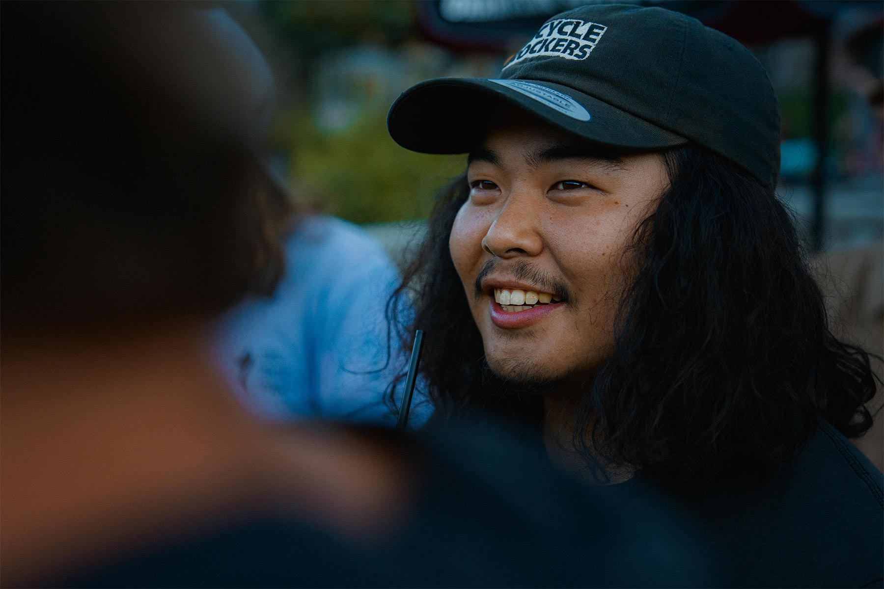 man smiling by the camera with a black hat on and his hair down