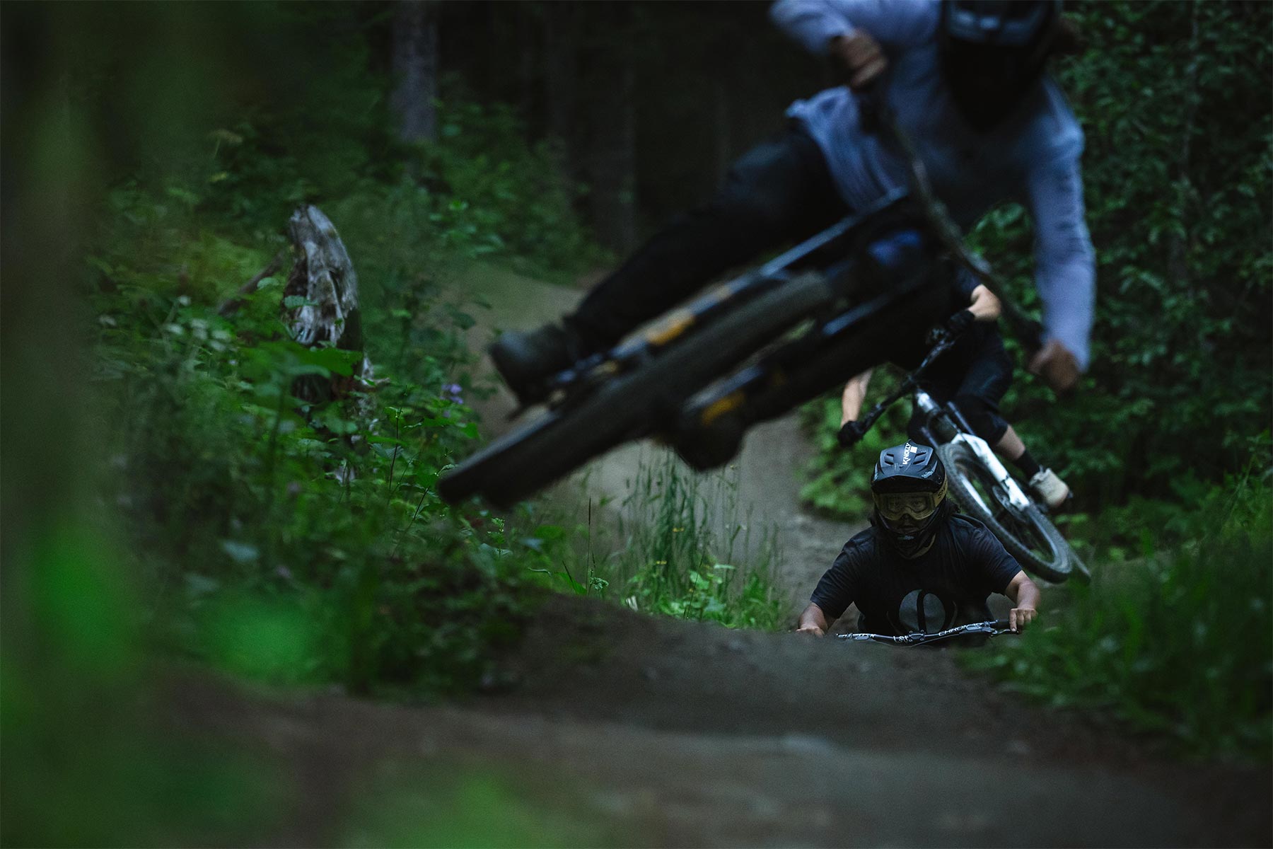 Three bikers in a line hitting a jump at dusk