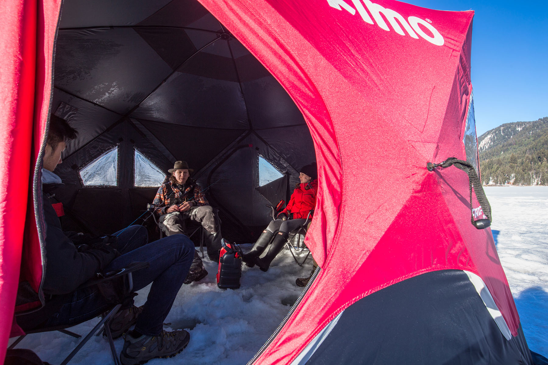 Group of three sitting in a tent on a frozen lake ice fishing.