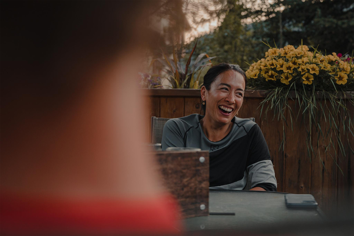 Kelly smiles at a table on a restaurant patio in the mountains in Summertime