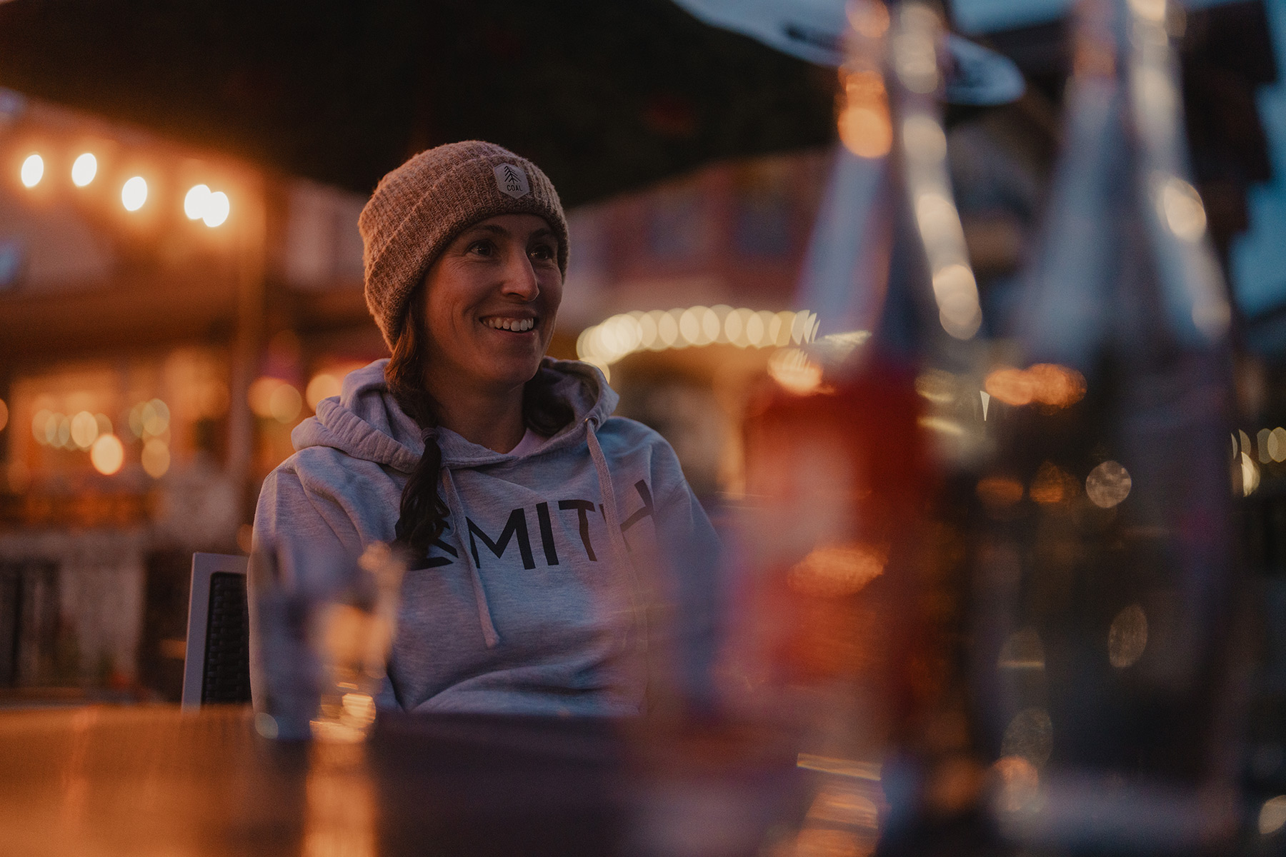 A woman in a toque smiles on an outdoor patio at night.