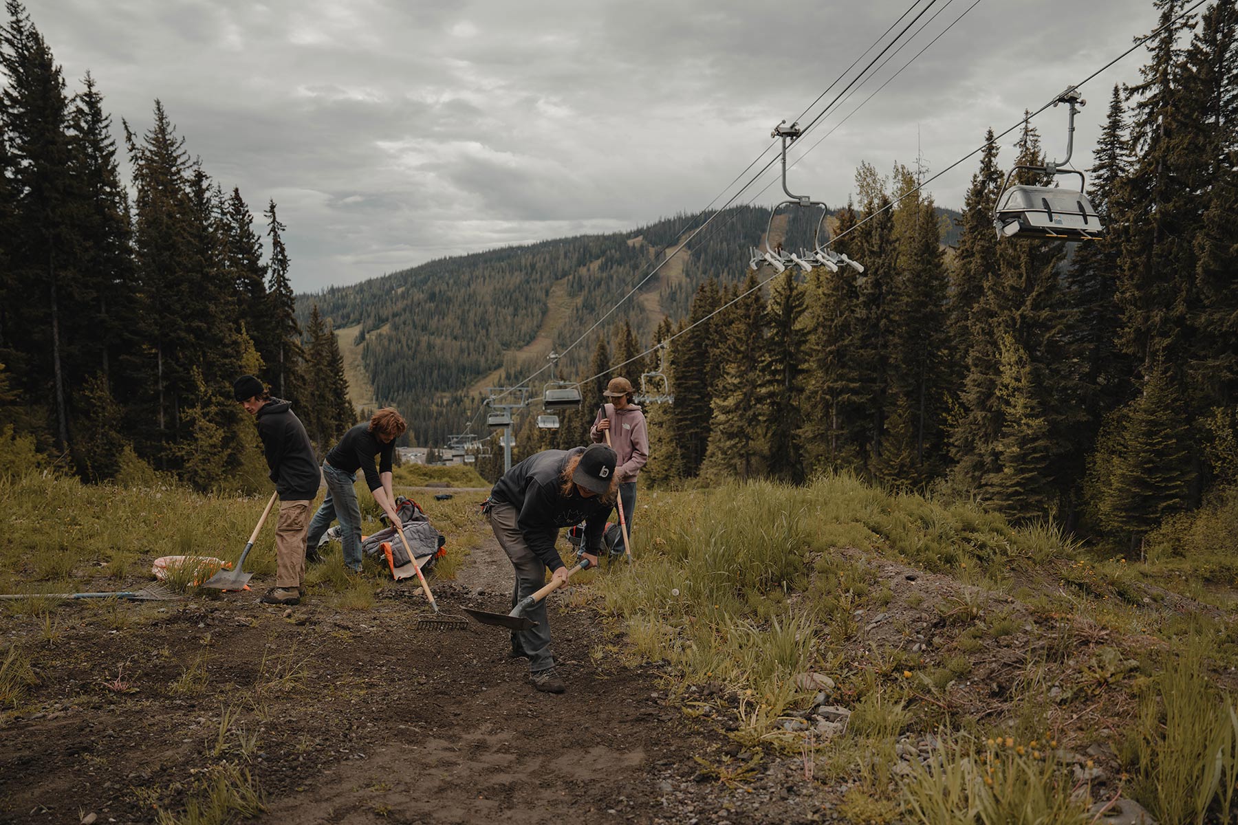 Four trail crew members work on a mountain bike trial with the chairlift in the background.