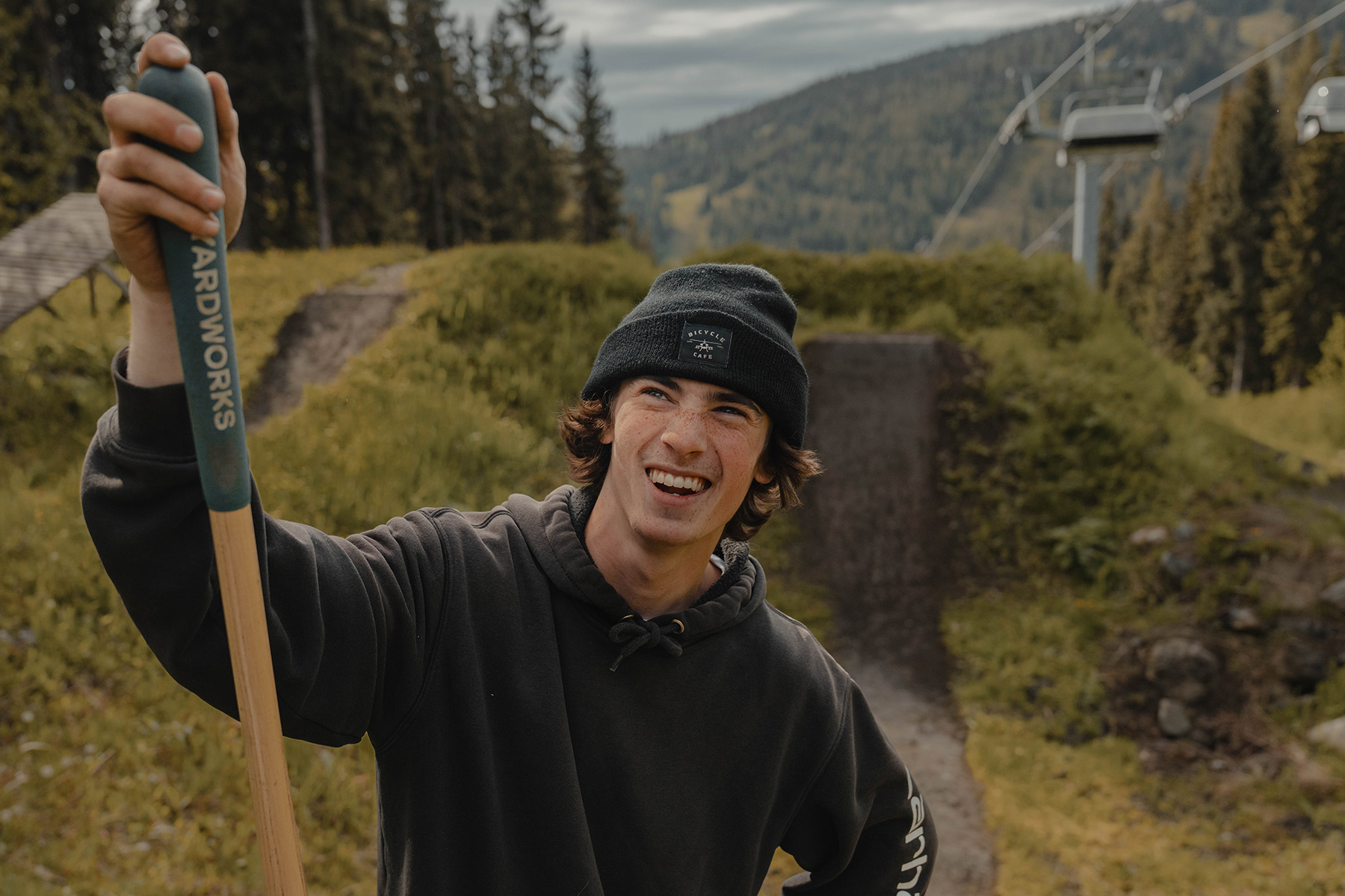 A trail builder looks up and smiles, holding the handle of a shovel.