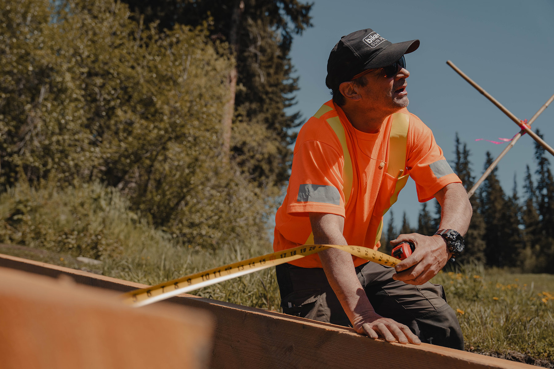A trail builder in high visibility clothing measures a wood beam.