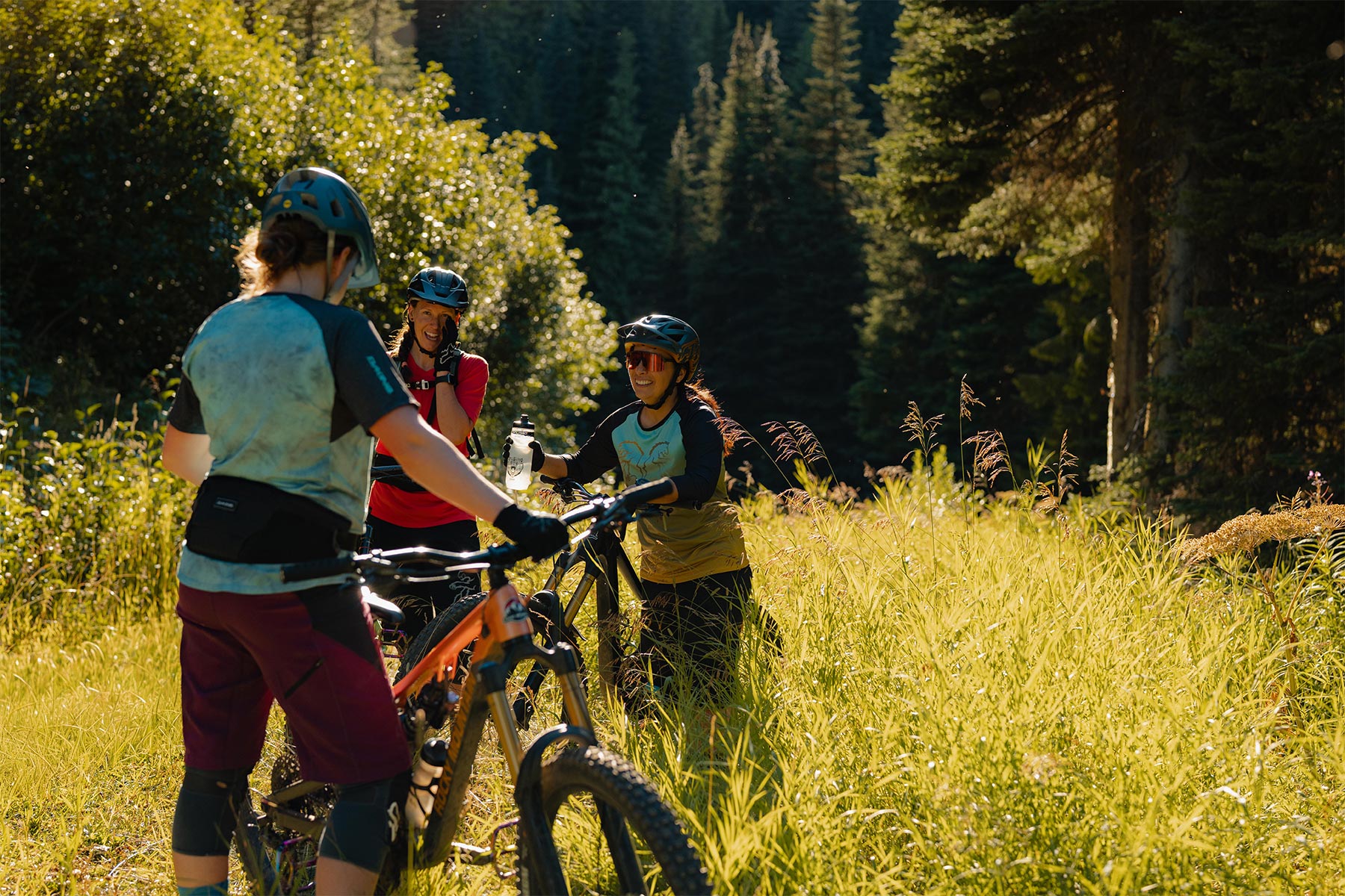 Three women standing in the grass with their bikes laughing and smiling