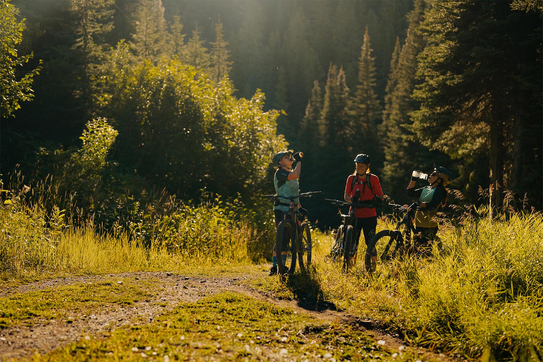 Two women drinking from their water bottles and one woman smiling in the trees