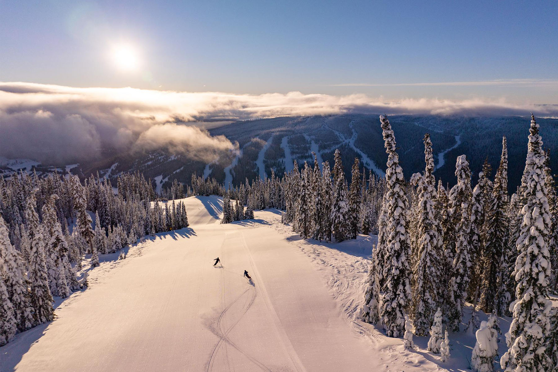 Wide open groomer run with two skiers.