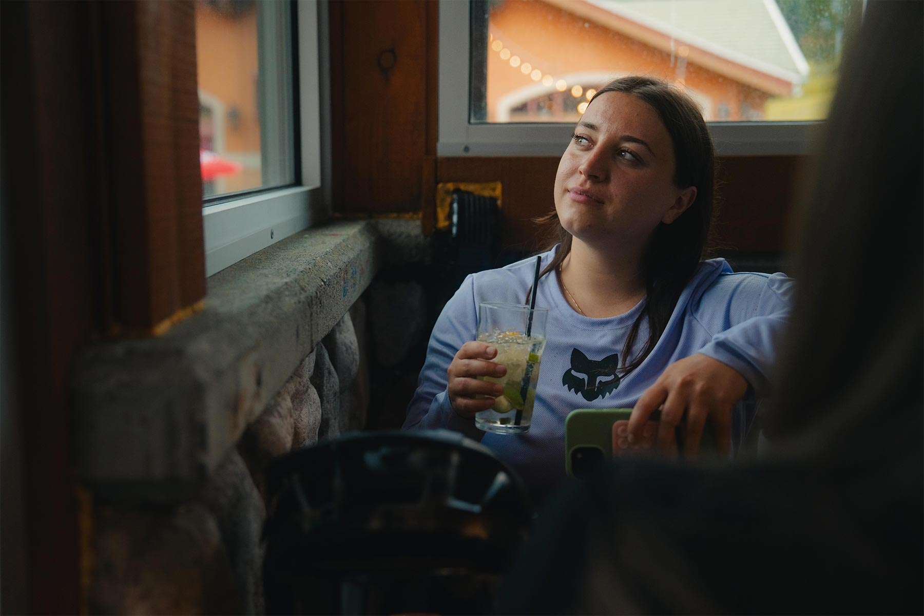 a girl holding a drink and looking out the window