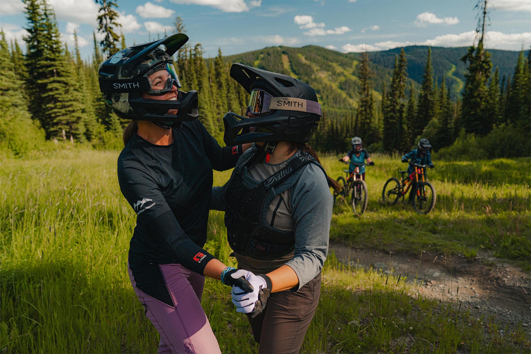 two girls dancing in the grass while two stand with bikes watching